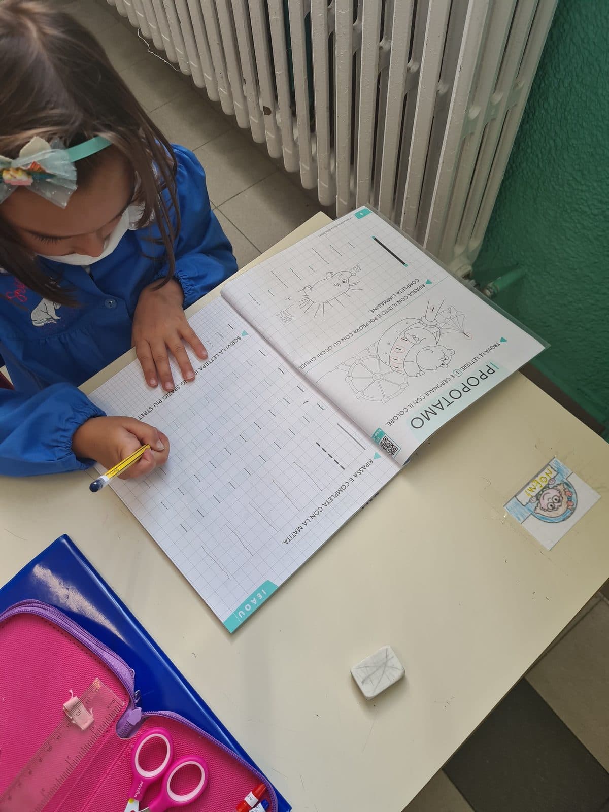 Une enfant écrit dans son cahier d'écriture, à sa table de classe.