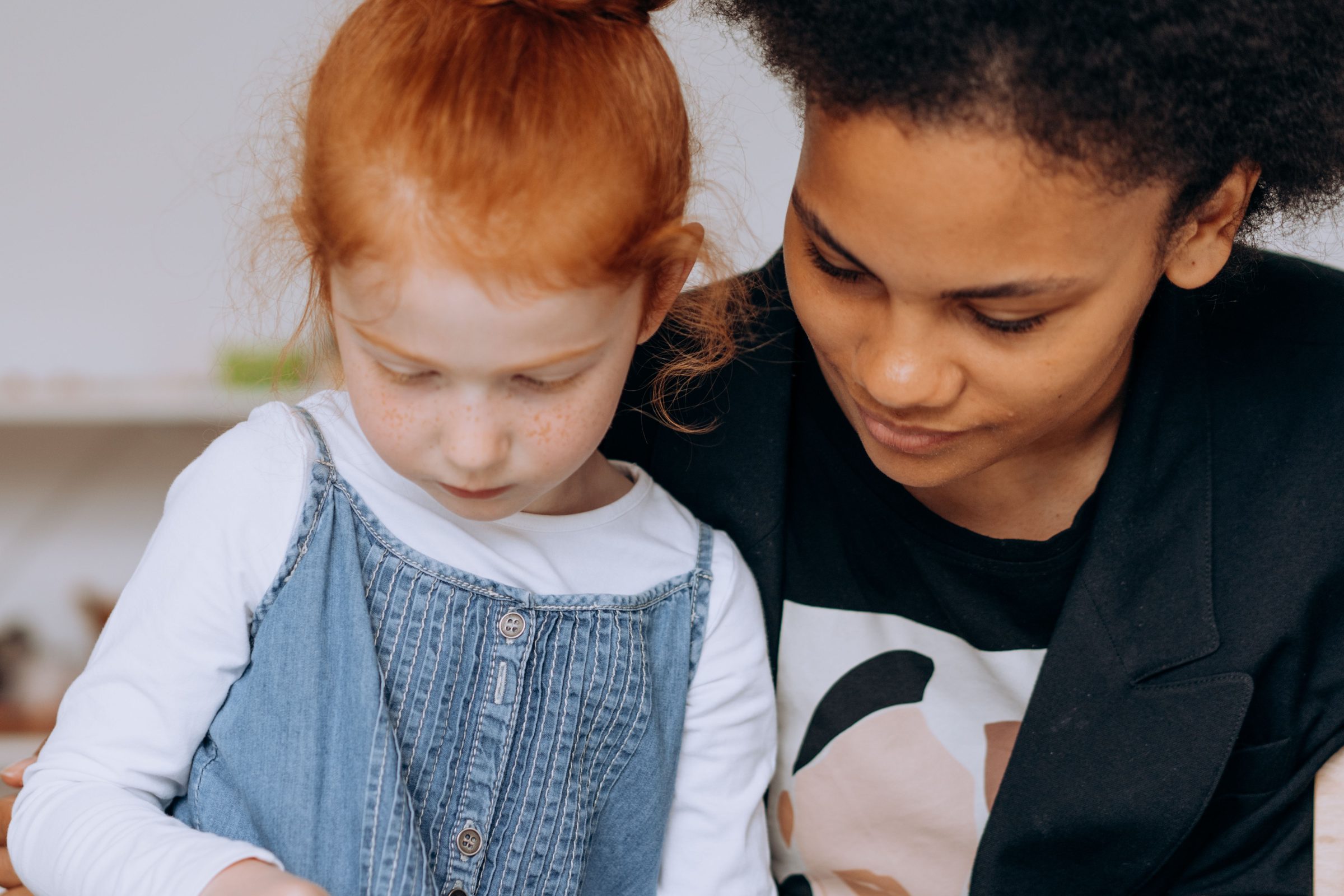 Éducatrice penchée aux côtés d'une petite fille, toutes deux concentrées sur une activité